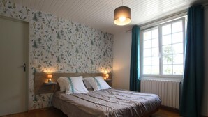 Un dormitorio con cama de madera, dos lámparas de noche, un ventanal con cortinas y una lámpara de techo.