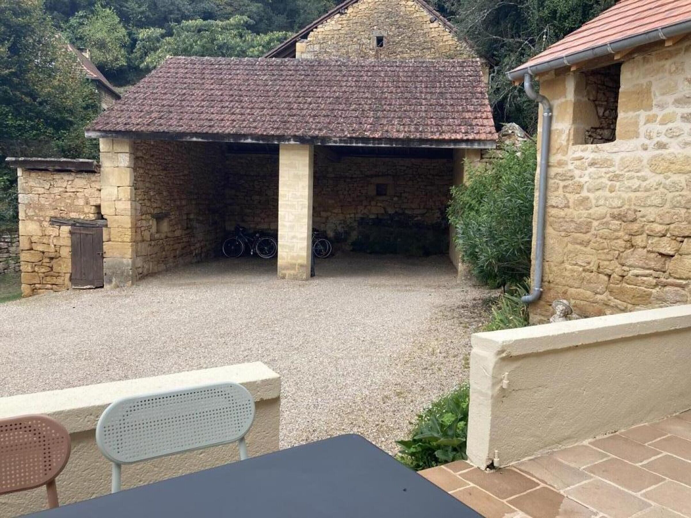 A stone building with a tiled roof, a gravel driveway, and a table with chairs outside.