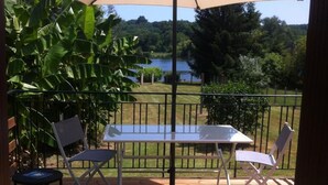 A patio with a table and chairs, surrounded by a railing, overlooking a lake and greenery. - Dordogne Getaway: Riverside House with Private Parking (Mauzac-et-Grand-Castang)