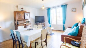 A living room with a dining table, chairs, a sofa, a television, and a cabinet with decorative items. - Dordogne Getaway: Riverside House with Private Parking (Mauzac-et-Grand-Castang)