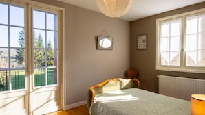 A bedroom with a bed, a chair, a lamp, a window with a view of greenery, and a hanging light fixture. - Dordogne Getaway: Riverside House with Private Parking (Mauzac-et-Grand-Castang)