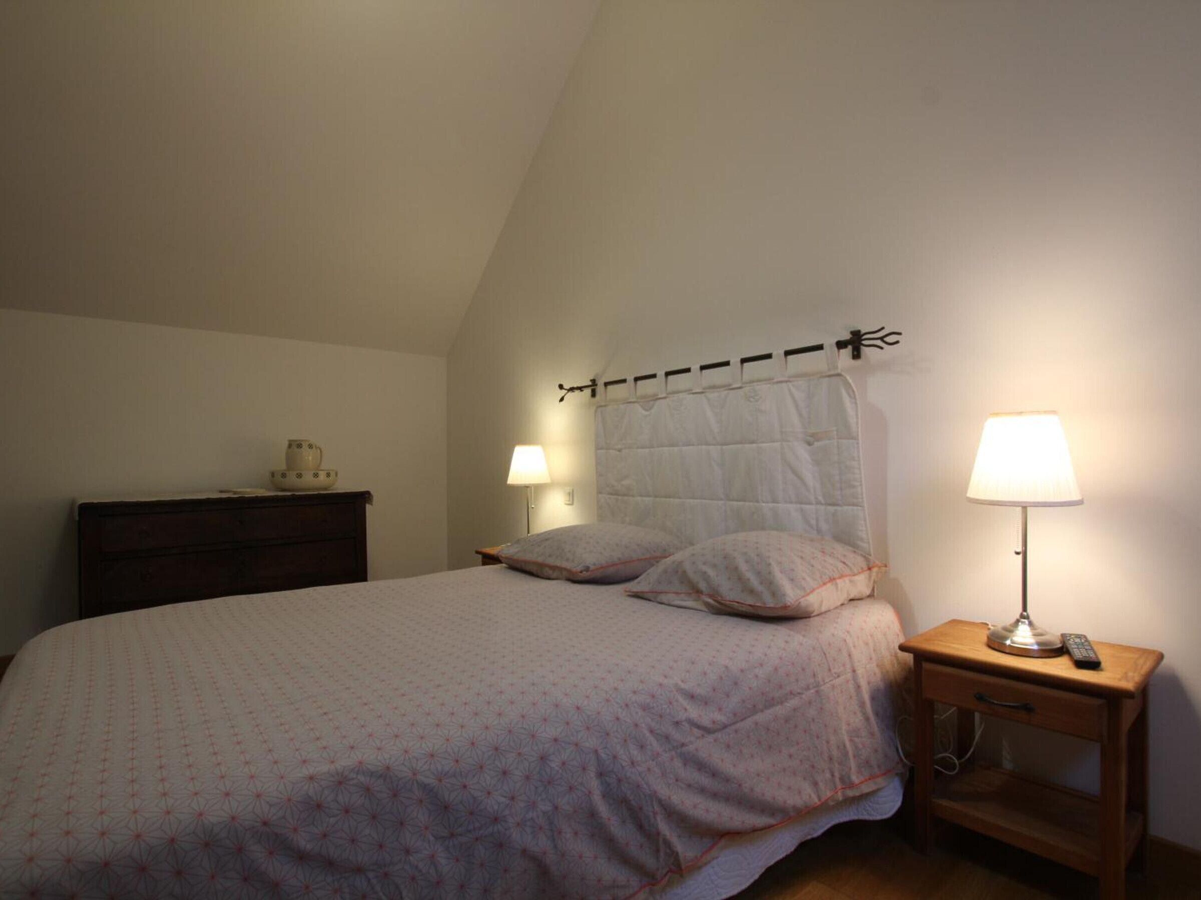 Une chambre à coucher comprenant un lit, deux lampes de chevet, une table de chevet et une commode.