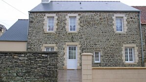 Une maison en pierre avec un toit en tuiles, une porte d’entrée et deux fenêtres au deuxième étage.