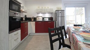 Une cuisine moderne équipée d’appareils électroménagers en acier inoxydable, un coin repas avec une table dressée pour deux personnes, et une vue sur l’extérieur.