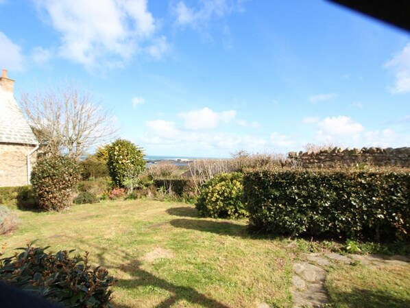 A garden with a stone wall, a hedge, and a view of the sea. - Cozy house in Auderville with sea view, near trails (La Hague)