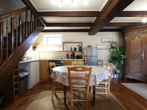 A cozy kitchen with wooden beams, a dining table with chairs, a refrigerator, and a sink.