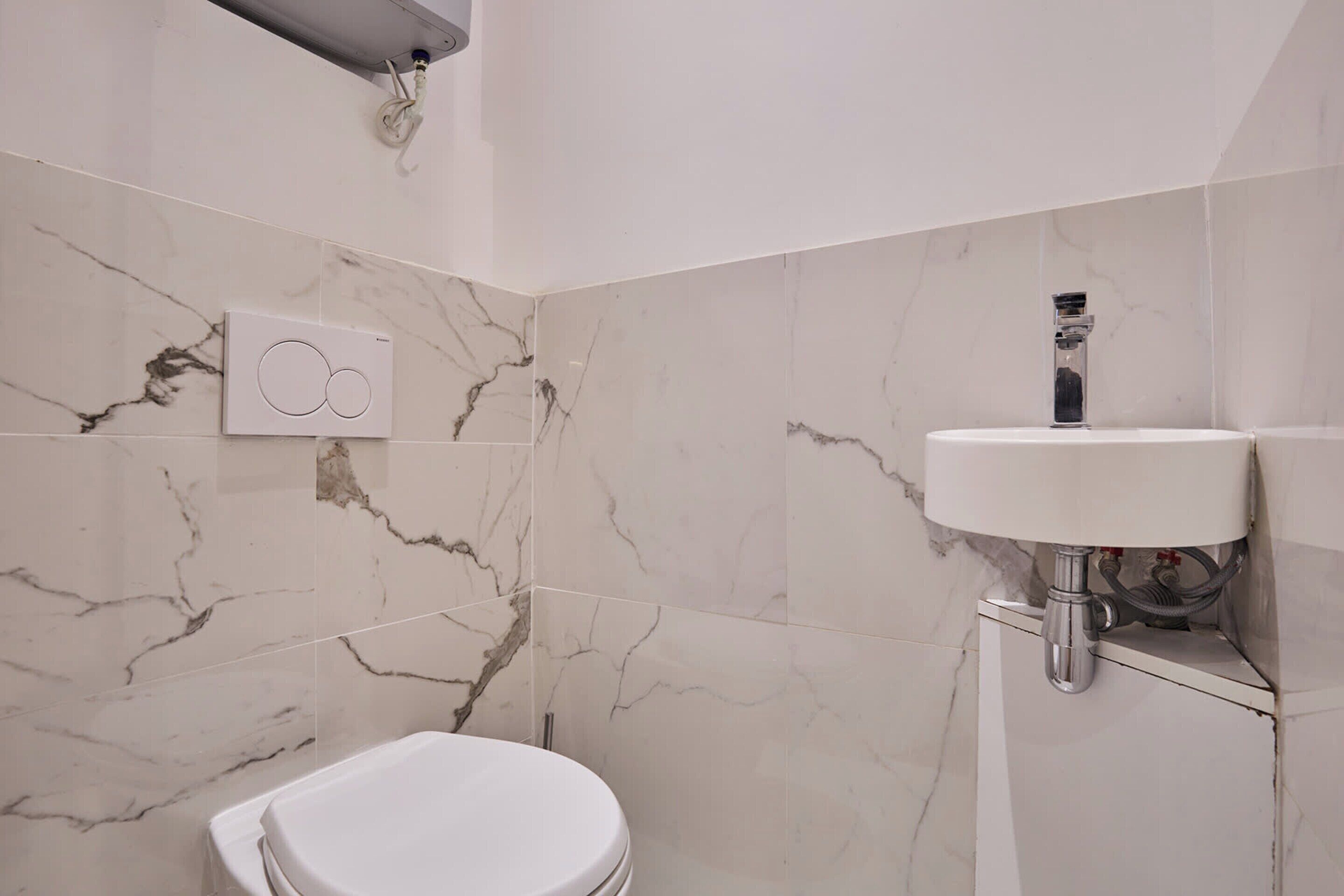 Un bagno con il water, un lavabo fissato alla parete e una parete con motivo marmorizzato.