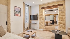 A modern living room with a stone wall, a flat-screen TV, a wooden coffee table, and a sofa. - The Upper Marais Superb Apartment for 8 People (Paris)