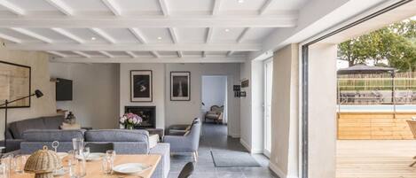 Et moderne spiseområde med et træbord dækket til fire personer, grå sofaer og udsigt til terrassen.