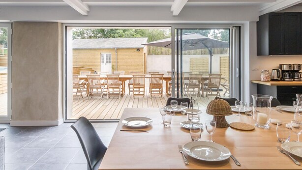 A modern kitchen with dark cabinets, a wooden dining table set for four, and a view of an outdoor patio area. - Spacious house with heated pool and garden, near beaches (Bricqueville-sur-Mer)