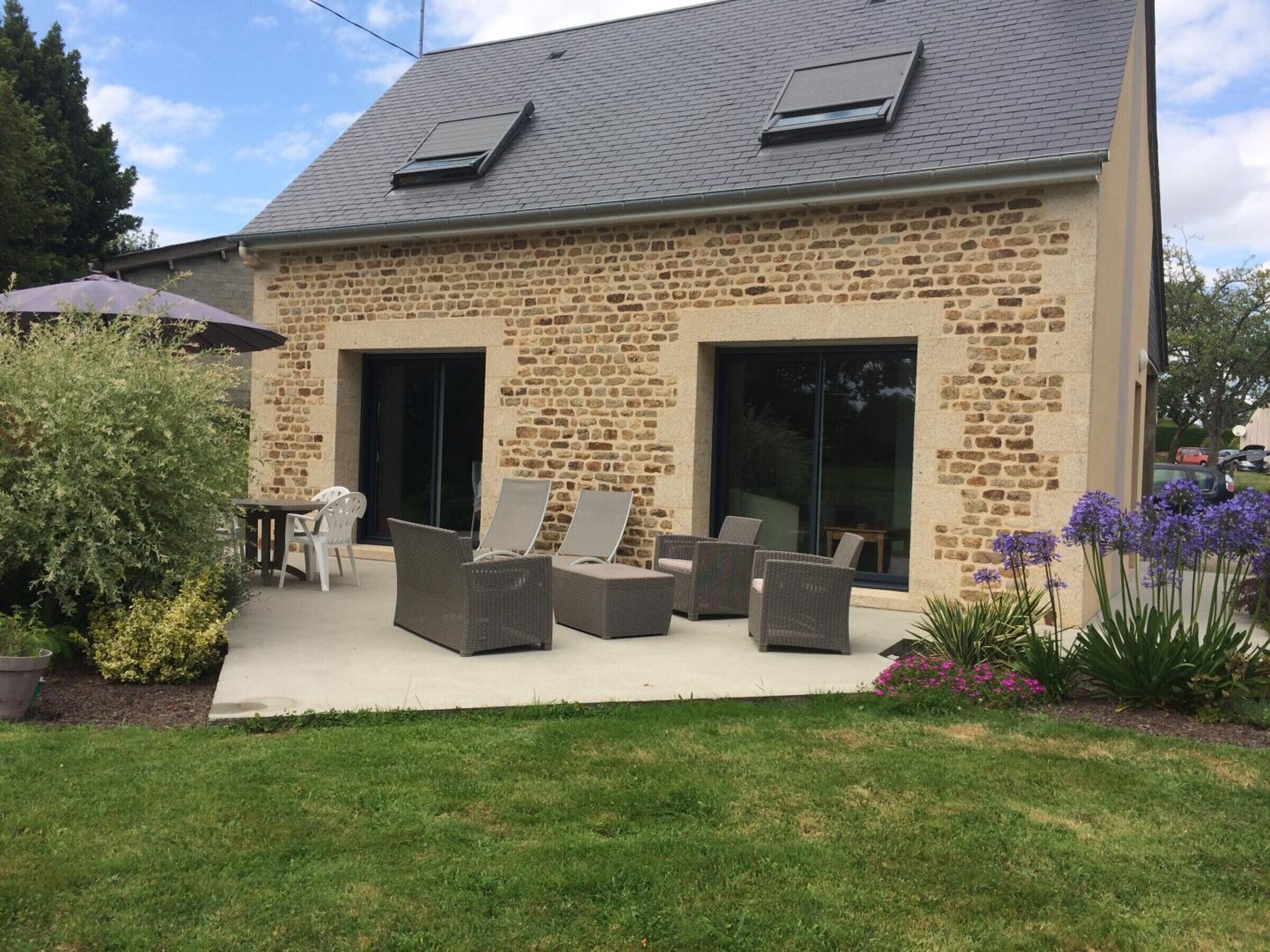 A stone building with a patio area featuring wicker furniture and a covered table.