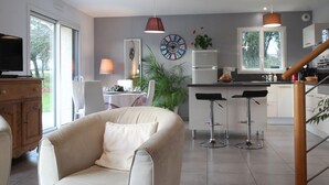 A modern kitchen with a refrigerator, stove, and bar stools. There is a dining area with a table and chairs.
