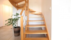 A wooden staircase with a handrail, leading to an upper floor. A potted plant is visible on the landing.