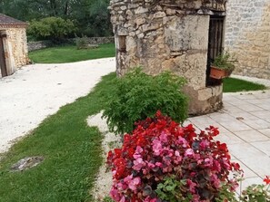 Un bâtiment en pierre doté d’une porte et d’une fenêtre, entouré d’un chemin de gravier et d’une pelouse verdoyante.