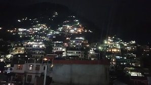 A nighttime view of a densely populated hillside with numerous buildings illuminated. - Hotel Aaditya (Kullu)