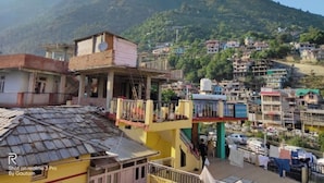 A residential area with multi-story buildings, a prominent yellow structure with a balcony, and a mountainous backdrop. - Hotel Aaditya (Kullu)