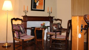 A room with two wooden chairs, a small table with a vase, a floor lamp, and a fireplace with two candles.