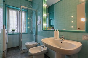 A bathroom with a glass shower enclosure, a toilet, a bidet, and a sink with a mirror above it. - Cinema & Bamboo Flats by Wonderful Italy (Turin)