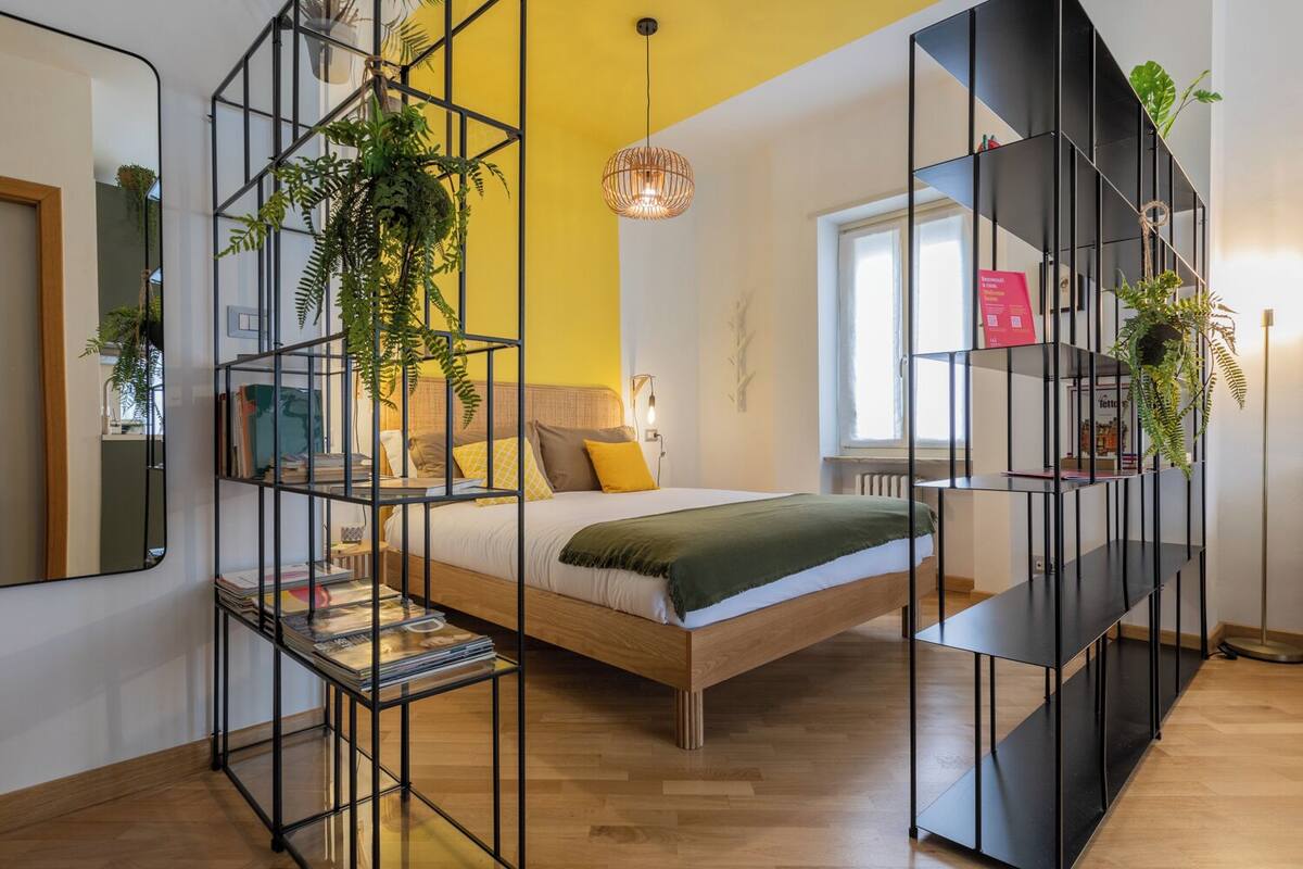 A modern bedroom with a bed, a bookshelf, and a hanging plant.