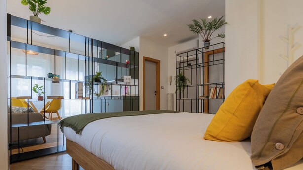 Un dormitorio moderno con una cama grande, un escritorio y una estantería con plantas.