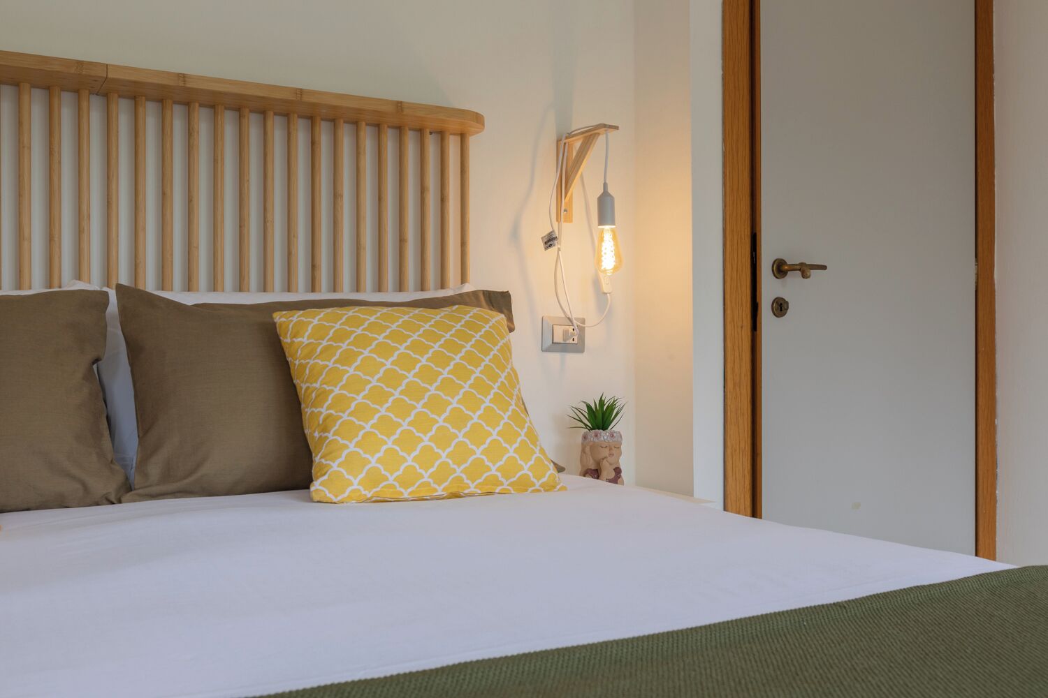 A neatly made bed with two pillows, a bedside lamp, and a small plant on the nightstand.
