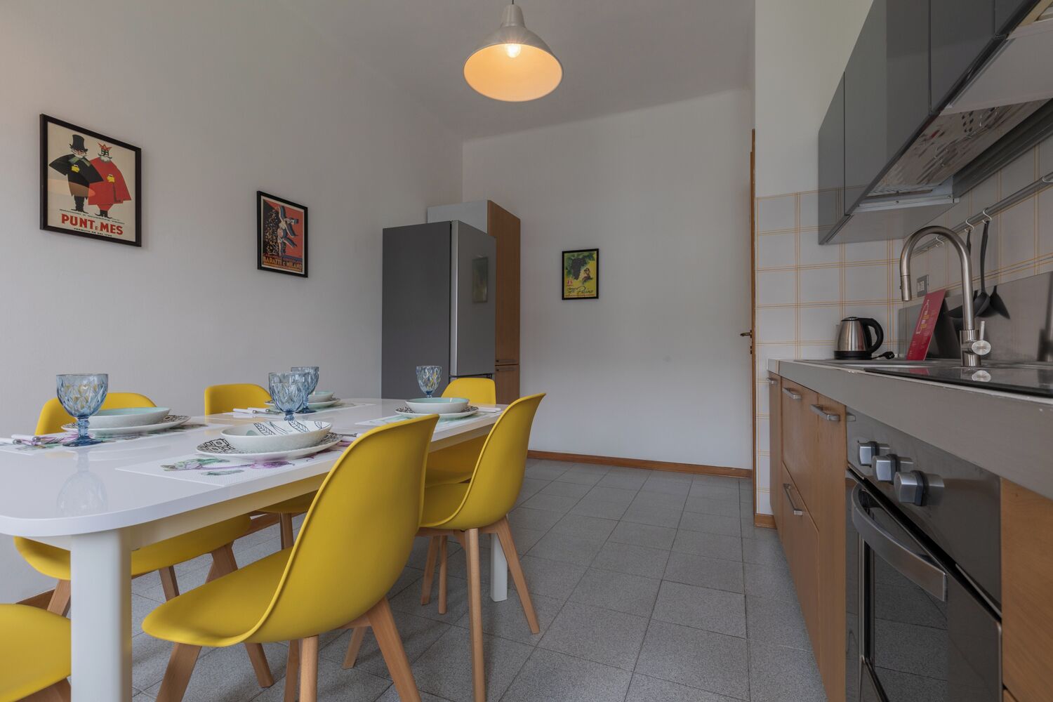 A dining area with a white table, yellow chairs, and a modern kitchen with stainless steel appliances.