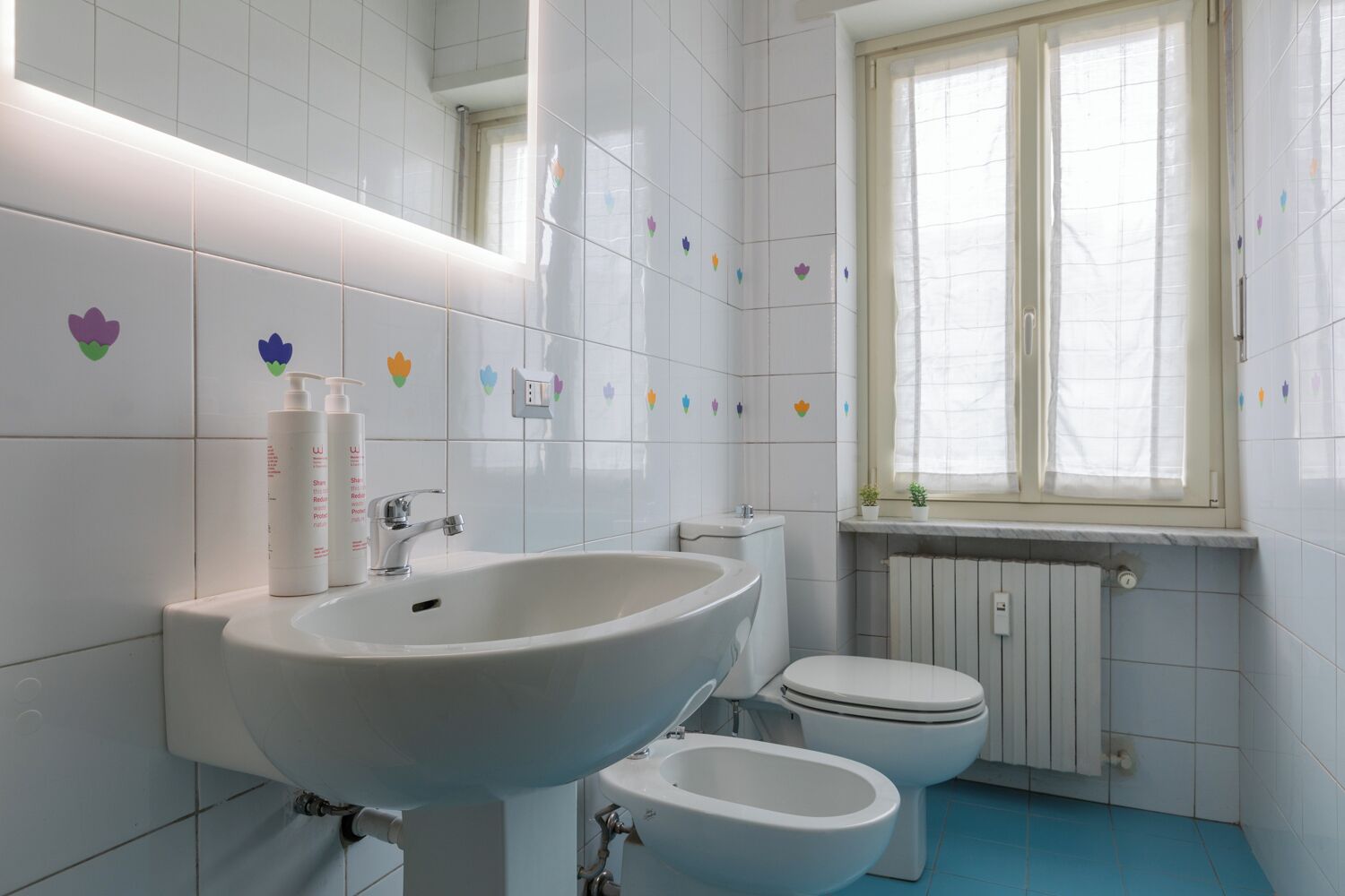 A bathroom with white tiles, a sink, a toilet, and a bidet.