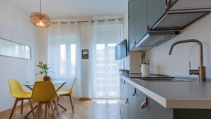 Cocina moderna con estufa integrada, un lavamanos y un televisor montado encima. Hay un comedor con una mesa y sillas, y una planta en maceta sobre la mesa.