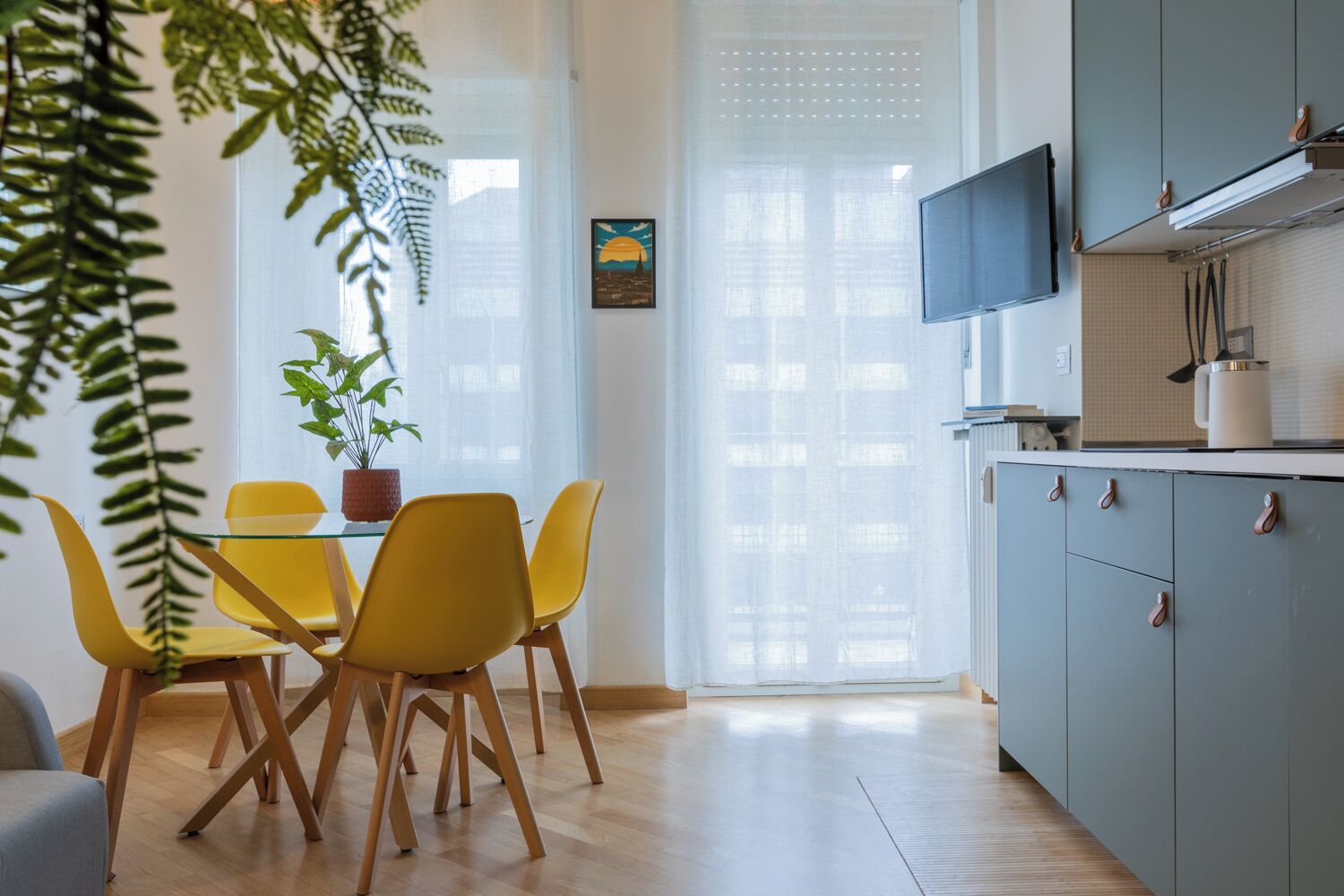 Een moderne keuken met een eethoek, met een tafel en stoelen, een potplant en een tv die boven de kasten is bevestigd.