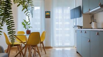 Een moderne keuken met een eethoek, met een tafel en stoelen, een potplant en een tv die boven de kasten is bevestigd.