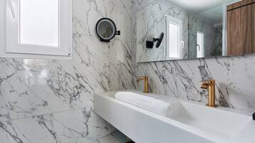 A modern bathroom with a marble backsplash, a large mirror, a white sink with gold faucets, and a towel on the counter.