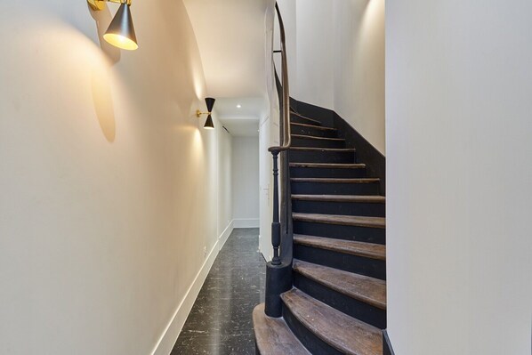 A modern staircase with a wooden handrail and black steps, leading to a landing with a white wall and a black floor.