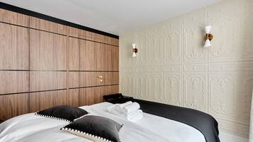 Habitació d'hotel amb un panell de fusta al capçal del llit, un llit amb roba de llit blanca, dues làmpades fixades a la paret i un panell decoratiu a la paret.