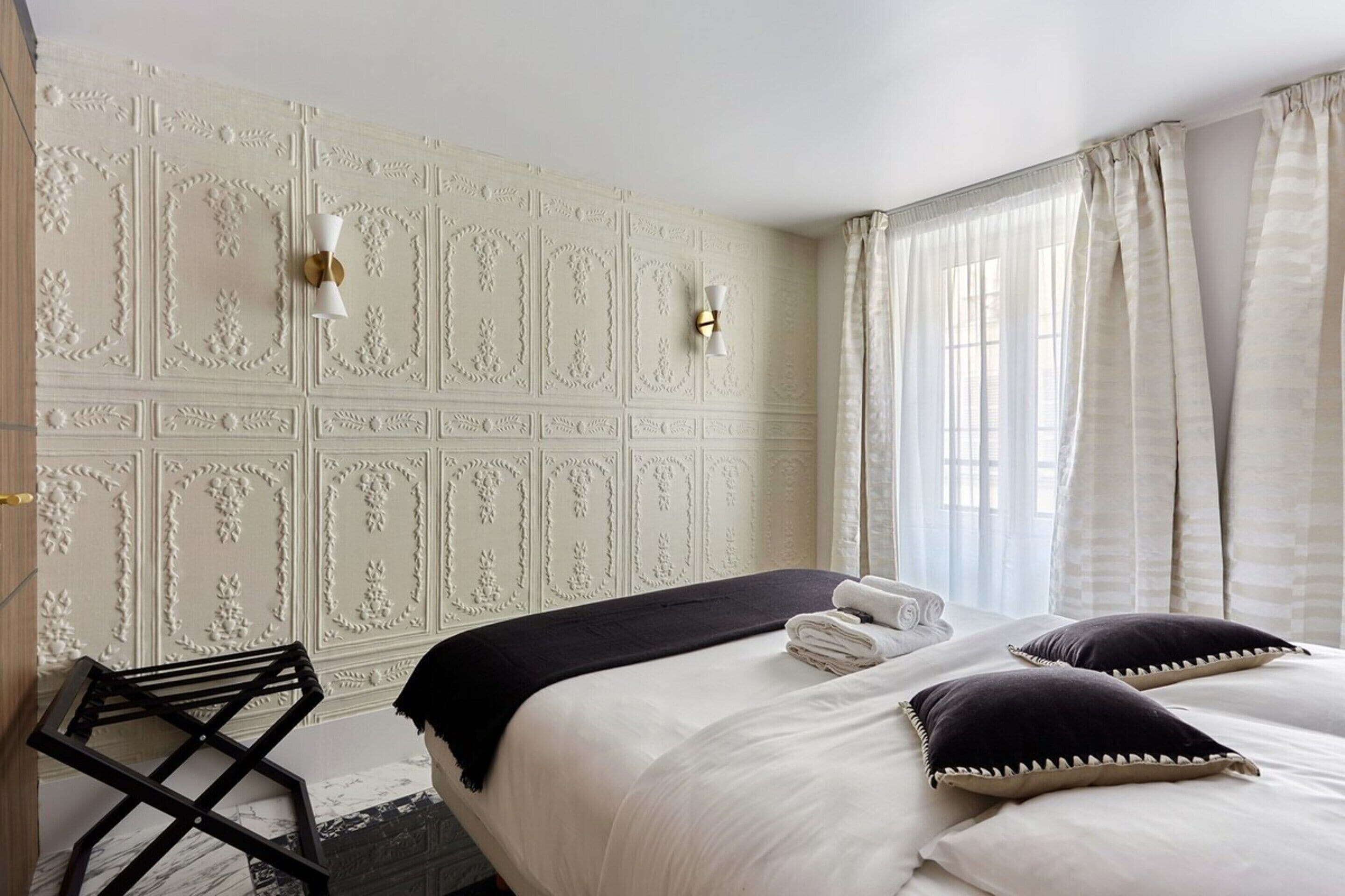 A hotel room with a bed, a chair, a decorative wall, and a window with curtains.