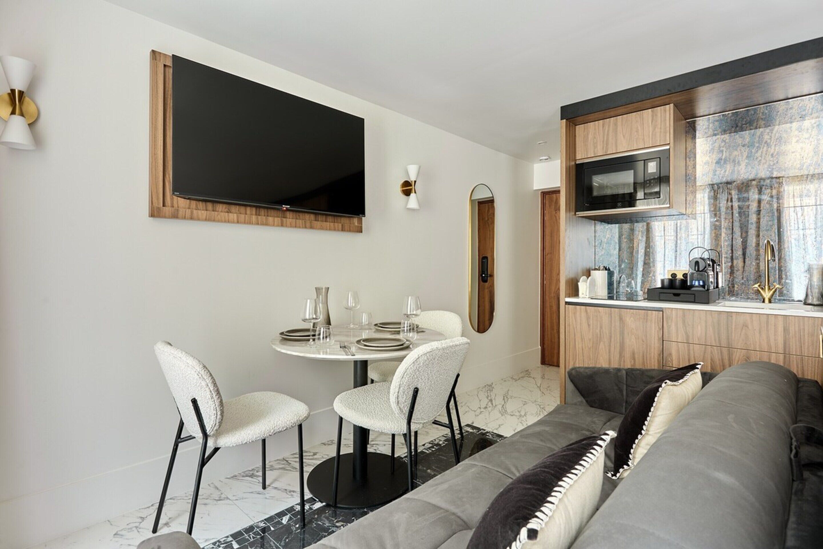 A compact living space with a dining area, a sofa, a television, and a kitchen area with a microwave.