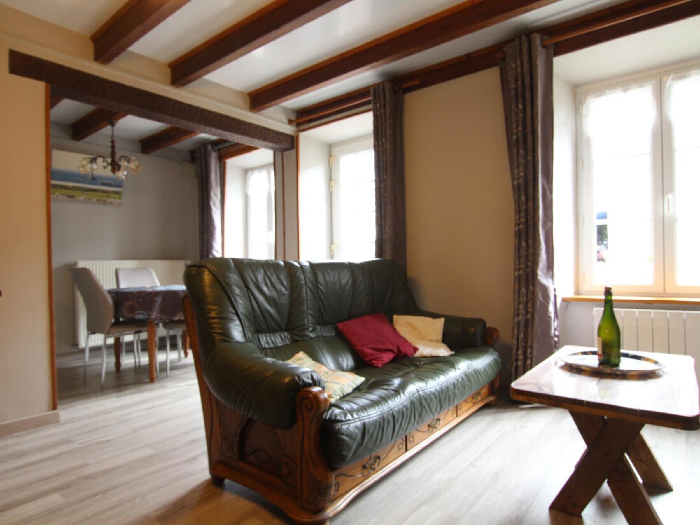 Ein Wohnzimmer mit Ledersofa, Holzbalken, einem Esstisch und Blick durch ein Fenster.