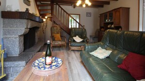 Una sala de estar acogedora con chimenea, un sofá de cuero verde, una mesa de centro de madera y una escalera que sube a otro nivel.