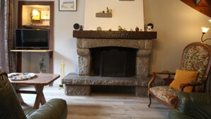 Una sala de estar acogedora con chimenea de piedra, un televisor sobre un mueble bajo, un sillón estampado y una escalera de madera.