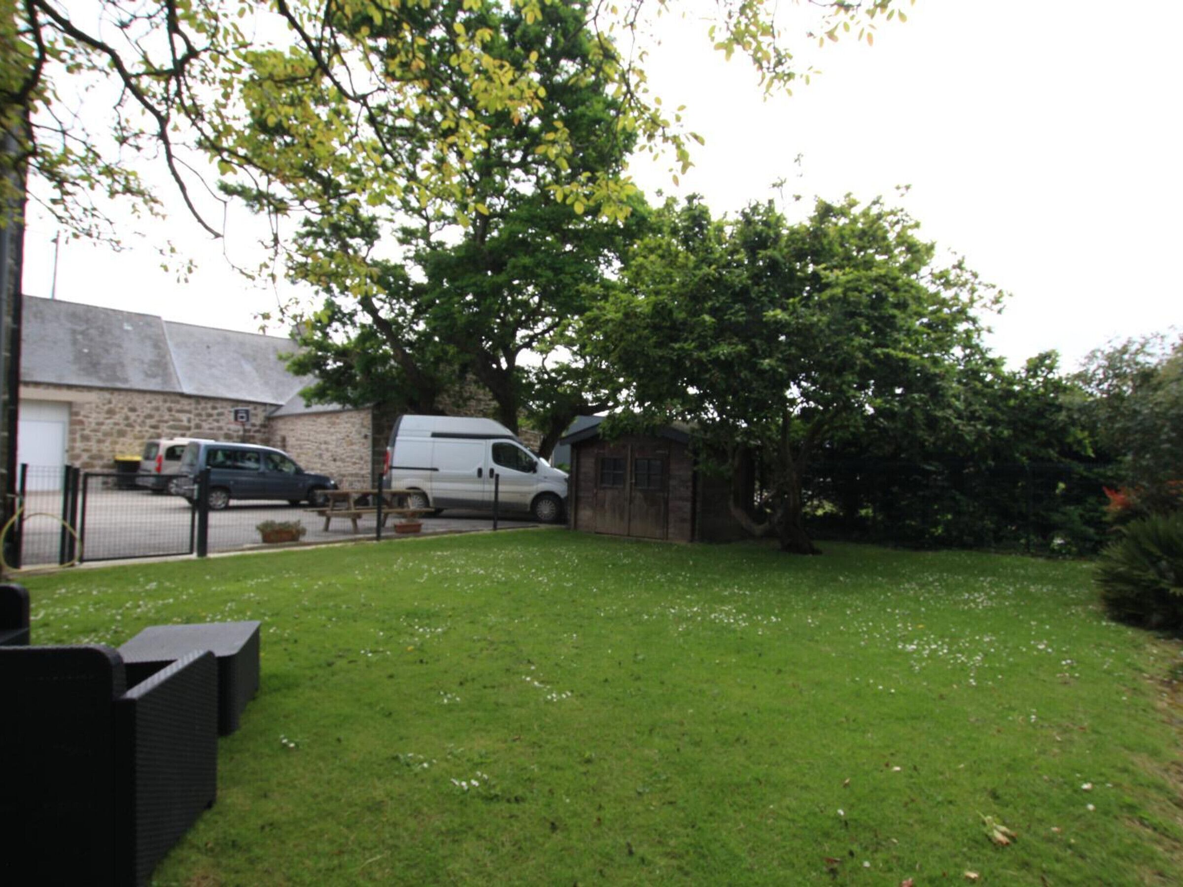 A residential area with a grassy lawn, a stone building, and parked vehicles.
