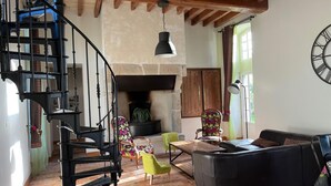 A spacious living room with a black staircase, a fireplace, a sofa, and a dining table.