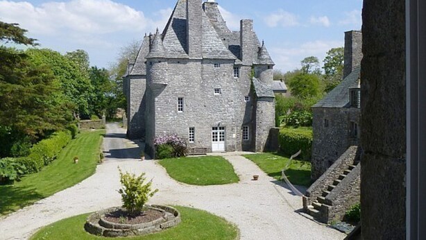 A stone castle with a central courtyard, surrounded by lush greenery and a well-maintained lawn.