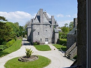 A stone castle with a central courtyard, surrounded by lush greenery and a well-maintained lawn. - Les Ecuries: Cotentin Cottage with pool, billiards, fireplace, 5 bedrooms (Bricquebosq)
