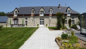 A large stone building with a central entrance, a covered patio area, and a well-maintained lawn.