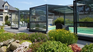 A modern outdoor patio with glass enclosures, a pool, and a well-maintained garden.