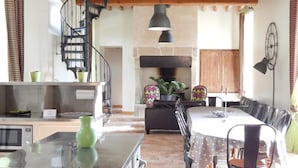 A spacious kitchen with a central island, a dining area with a large table and chairs, and a spiral staircase leading to an upper level.