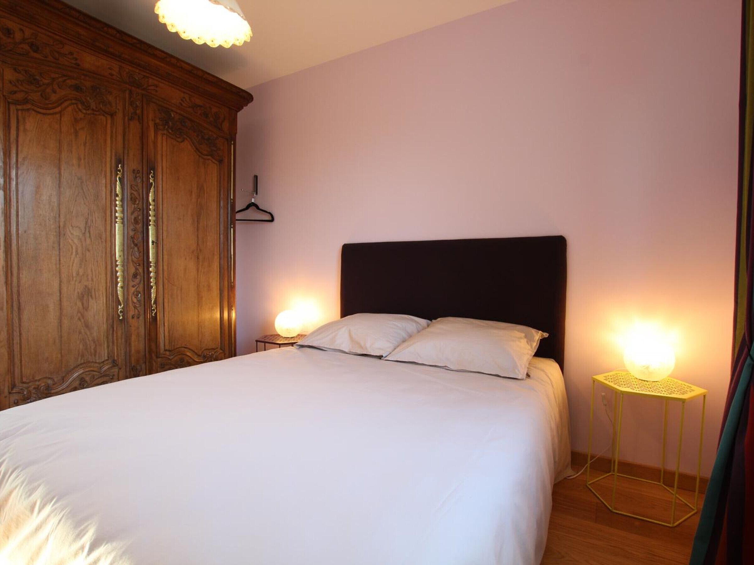 Camera da letto con un letto grande, un'armadio in legno, lampade sui comodini e un tavolino.