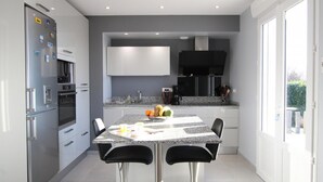 A modern kitchen with a granite countertop, stainless steel appliances, and a dining area with two bar stools. - House in Gratot, near beaches, WIFI, parking (Gratot)