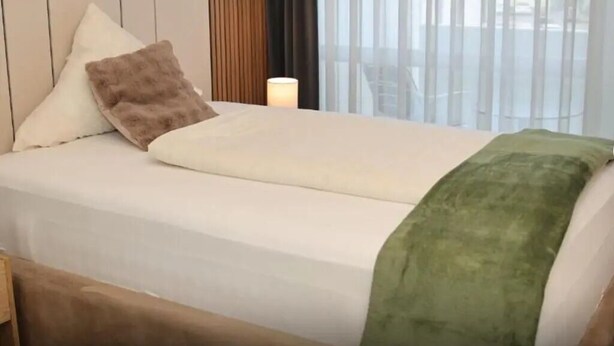 Ein Hotelzimmer mit Bett, Nachttisch, Lampe und einem Fenster mit Vorhängen.