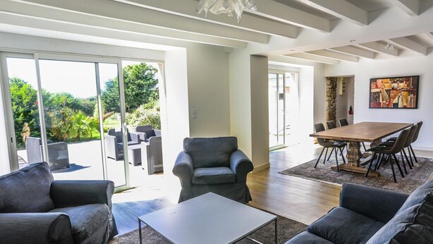 Amplia sala de estar con diseño moderno, que incluye una gran mesa de comedor, asientos cómodos y vistas a un patio exterior a través de puertas de cristal.