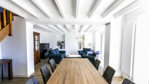Un salón espacioso con una larga mesa de madera, sofás oscuros y una chimenea moderna.